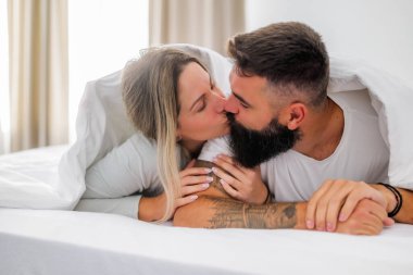Genç ve mutlu bir çift sabahları yatakta yatıyor. Eğleniyorlar ve öpüşüyorlar..