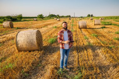 Çiftçi saman balyalarının yanında duruyor. Hasadı başarıyla tamamladıktan sonra samanı inceliyor..