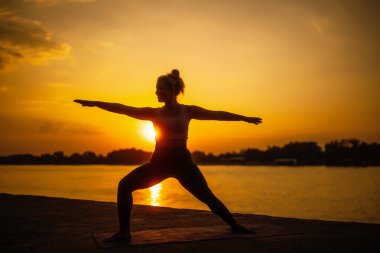 Woman practicing yoga in sunset. Virabhadrasana, Warrior 2 pose. clipart