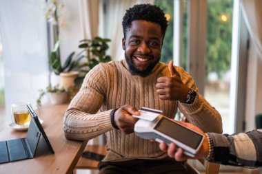 Rahat bir kafede otururken, günlük giysiler içinde genç bir adam kredi kartıyla temas kurmadan ödeme yapıyor..