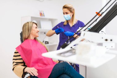 Mutlu dişçi ve hasta konuşuyor ve gülümsüyor. Modern dişçi kliniğinde dişçilik sınavı.