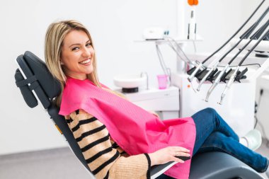 Modern diş kliniğinde mutlu genç bir kadın. Kameraya bakıyor ve gülümsüyor..