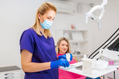 Dişçi genç bir kadının dişlerini onarıyor. Diş dolgusu hazırlıyor..