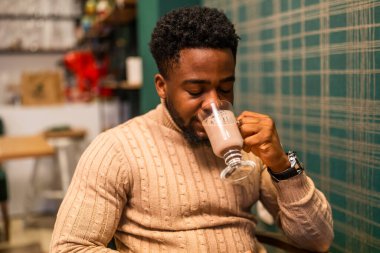 Barda sıcak çikolatanın tadını çıkaran genç bir zenci. Sıcak çikolata içen adamın portresi..