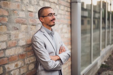 Tuğla duvarın önünde duran genç işadamının portresi, başka yere bakıyor ve düşünüyor..