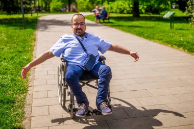 Tekerlekli sandalyedeki mutlu adamın portresi. Şehir parkında güneşli bir günün tadını çıkarıyor..