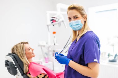 Dişçi hastanın dişlerini onarıyor. Dişlerini kontrol ettiren ve tamir ettiren genç bir kadın..