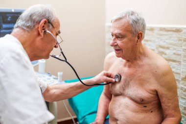 Hastanın kardiyologda muayenesi var. Doktor kalp atışlarını ve akciğerlerinin sesini dinliyor..