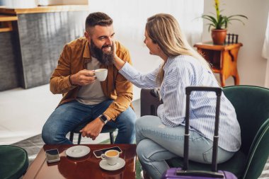 Neşeli evli çift otele geldi. Tatildeler, bavullarıyla lobide oturuyorlar, kahve içip eğleniyorlar..