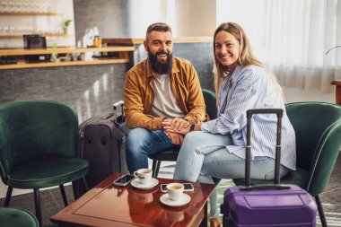 Mutlu evli çift otele geldi. Tatildeler, bavullarıyla lobide oturuyorlar, kameraya bakıyorlar ve gülümsüyorlar..