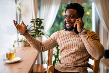 Neşeli siyah bir adam barda oturuyor, gündelik giyinmiş. Cep telefonuyla konuşuyor..