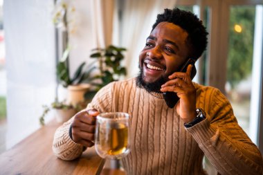 Genç siyah bir adam barda oturuyor, sıradan giyinmiş. Telefonda konuşuyor ve çay içiyor..