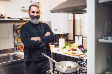 Restoranın mutfağında çalışan profesyonel şefin portresi. O bir yemek hazırlamaya hazır. Aşçı kollarını kavuşturup mutfakta duruyor..