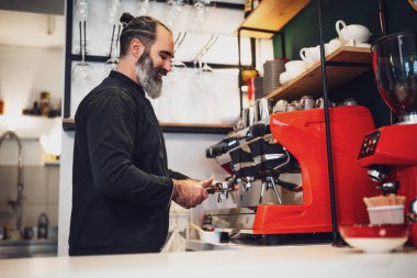 Restoranda çalışan siyah önlüklü profesyonel bir barista. Barında kahve yapan mutlu barmenlerin portresi..