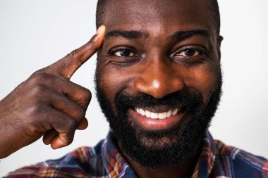 Mutlu siyah adam gülümsüyor ve kafasını işaret ediyor. Fikri olan bir adamın portresini kapat..