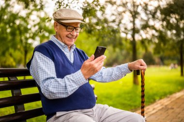 Park 'taki mutlu son sınıf öğrencisinin portresi. Bankta oturuyor ve akıllı telefon kullanıyor..