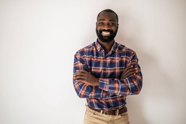 Kollarını kavuşturup gülümseyerek duvarda uzanan rahat gömlekli mutlu siyah adam..