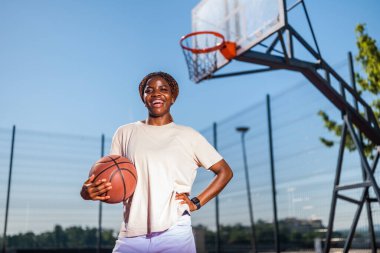 Genç bir kadın sabah spor salonunda tek başına basketbol oynuyor. Mutlu kız güneşli bir günde basketbol oynuyor..