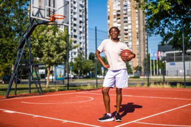 Genç bir kadın sabah spor salonunda tek başına basketbol oynuyor. Mutlu kız güneşli bir günde basketbol oynamaya hazır..