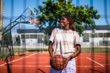 Genç bir kadın sabah spor salonunda tek başına basketbol oynuyor. Mutlu kız güneşli bir günde basketbol oynamaya hazır..