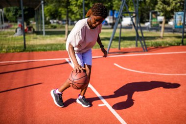 Genç siyahi kadın sabahları spor salonunda tek başına basketbol oynuyor. O, topu sürüyor..