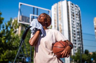 Genç siyah kadın basketbol sahasında duruyor. Yorgun ve terini siliyor..