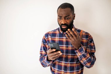 Rahat gömlekli endişeli siyah adam duvarın önünde dikiliyor ve akıllı telefondan video görüşmesi yapıyor..