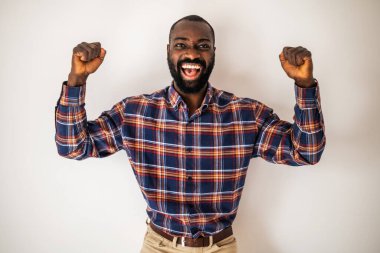 Hoş gömlekli neşeli siyah adam duvarın önünde duruyor ve gülümsüyor. Coşkuyla kollarını kaldırıyor..