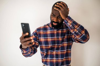 Rahat gömlekli endişeli siyah adam duvarın önünde dikiliyor ve akıllı telefondan video görüşmesi yapıyor..