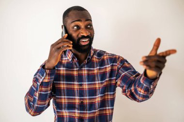 Rahat gömlekli neşeli siyah adam duvarın önünde duruyor ve cep telefonuyla konuşuyor..