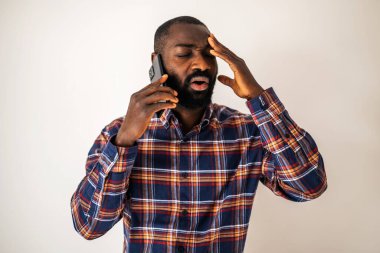 Endişeli ve yorgun, rahat gömlekli siyah adam duvarın önünde duruyor ve cep telefonuyla konuşuyor..
