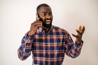 Rahat gömlekli kızgın siyah adam duvarın önünde duruyor ve cep telefonuyla konuşuyor..