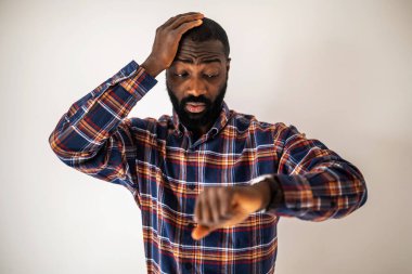 Rahat gömlekli endişeli siyah adam duvarın önünde duruyor ve kol saatine bakıyor. Geç kalacak..