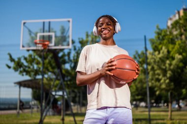 Genç bir kadın sabah spor salonunda tek başına basketbol oynuyor. Mutlu kız basketbol oynuyor ve güneşli bir günde müzik dinliyor..