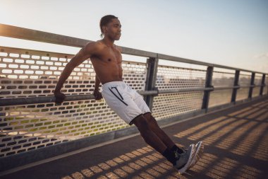 Genç Afro-Amerikalı adam, şehirdeki köprüde egzersiz yapıyor. Ters şınav çekiyor..