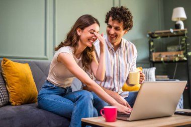 Yetişkin çift evdeki kanepede oturuyor ve dizüstü bilgisayar kullanıyorlar. İnternetten alışveriş yapıyorlar..