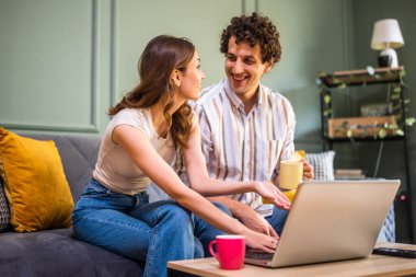 Yetişkin çift evdeki kanepede oturuyor ve dizüstü bilgisayar kullanıyorlar..