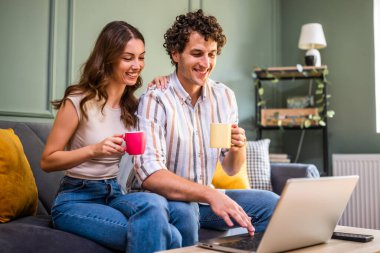 Yetişkin bir çift ailesiyle görüntülü görüşme yapıyor. Kadın ve erkek evdeki koltukta oturuyor ve dizüstü bilgisayar kullanıyorlar.. 