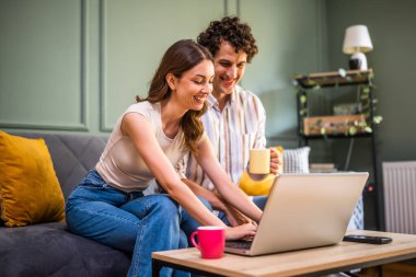 Yetişkin çift evdeki kanepede oturuyor ve dizüstü bilgisayar kullanıyorlar. Online alışveriş yapıyorlar ve mal arıyorlar..