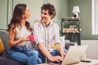Yetişkin bir çift ailesiyle görüntülü görüşme yapıyor. Kadın ve erkek evdeki koltukta oturuyor ve dizüstü bilgisayar kullanıyorlar..
