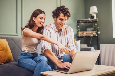 Yetişkin çift evdeki kanepede oturuyor ve dizüstü bilgisayar kullanıyorlar. Online alışveriş yapıyorlar ve mal arıyorlar..