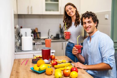 Yetişkin çift mutfaklarında smoothie hazırladı. Elektrikli sıkacağa karıştırılmış çeşitli meyveler kullandılar. Smoothie içiyorlar..