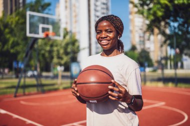 Afrika kökenli Amerikalı kadın oyuncu yaz antrenmanı sırasında top tutuyor ve gülüyor. Aktif yaşam tarzı ve şehir sporları.