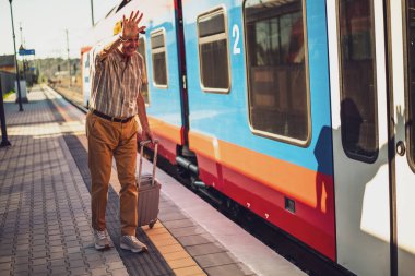 Senior man is arriving at railway station and is anxious to enter the train. Senior people traveling.