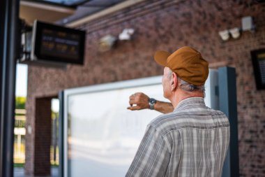 Portrait of senior man at train station. He is waiting for boarding and checking the departure time. Senior people traveling.