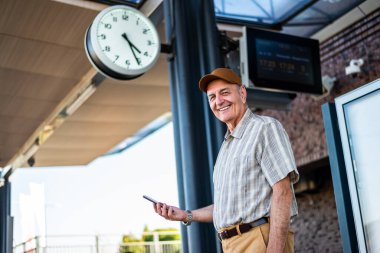 Portrait of happy senior man at train station. He is waiting for boarding. Senior people traveling.