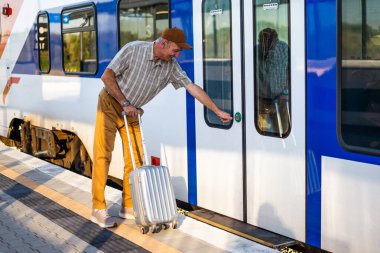 Senior man is boarding the train at railway station. Senior people traveling.