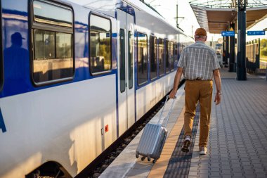 Senior man is arriving at railway station and is ready to enter the train. Senior people traveling.