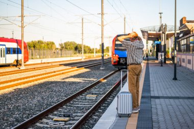 Senior man is standing at railway station. He missed the train departure and holding his head in disbelief. Senior people traveling.