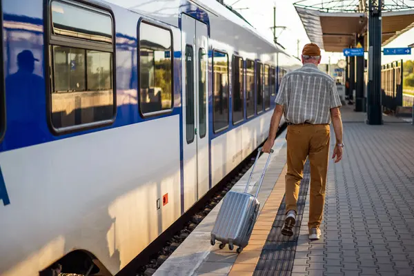 Senior man is arriving at railway station and is ready to enter the train. Senior people traveling.